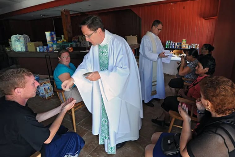The Rev. William Murphy (left) and the Rev. Joseph Devlin give communion during noon Mass at Mother of Mercy House, formerly a bar. (CLEM MURRAY/Staff Photographer)