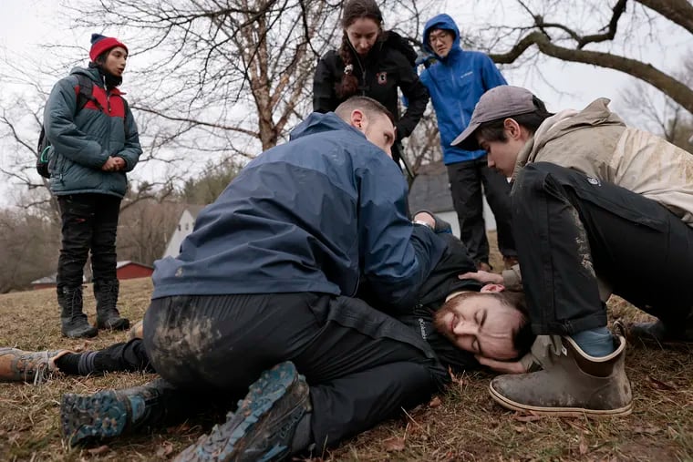 Penn medical student Andy North (lying on on ground) pretends to be the victim of a black bear attack as other students assess his condition. From left: Kiran Raja, Sam Stedman, Brooke Bernardin, Daniel Park, and Francisco Zepeda took part in the training exercise at Camp Shelly Ridge in Lafayette Hill.