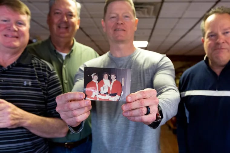 Joe Reichwein holds up a picture of three of the ten men who dressed up in Santa suits for the Sixers game December 12, 1984, while Mike Reichwein (left), Jay Barthelmess (second from left), and Mike Power (right) stand for a portrait while they reunited and reminisced at Chalfont Family Restaurant in Chalfont, PA, Saturday, March 16, 2019. This year is the 35th anniversary of the notable event, "The night Santas fought back".