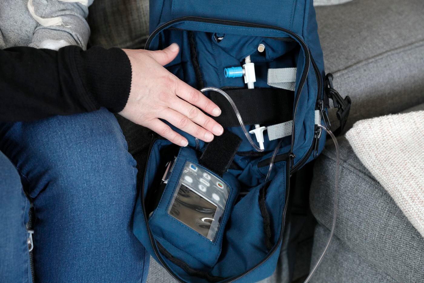 Lisa Oney displays the small over-the-the shoulder bag that delivers her intravenous chemotherapy treatment.