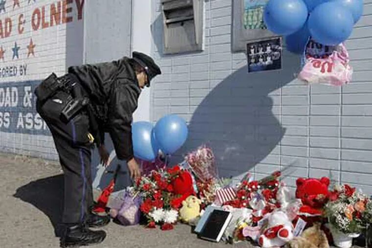 Officer Nannette Taylor from 35th district fixes a makeshift shrine at Broad and Olney Streets near where fellow officer John Pawlowski was slain Friday. (Akira Suwa / Staff Photographer ).