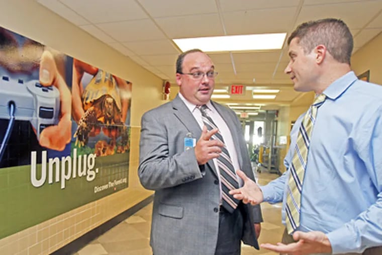 At Manor Elementary School in the Pennsbury District, principal Christopher Becker (right) and district Assistant Superintendent W. David Bowman talk in front of a large ad. (Akira Suwa / Staff Photographer)