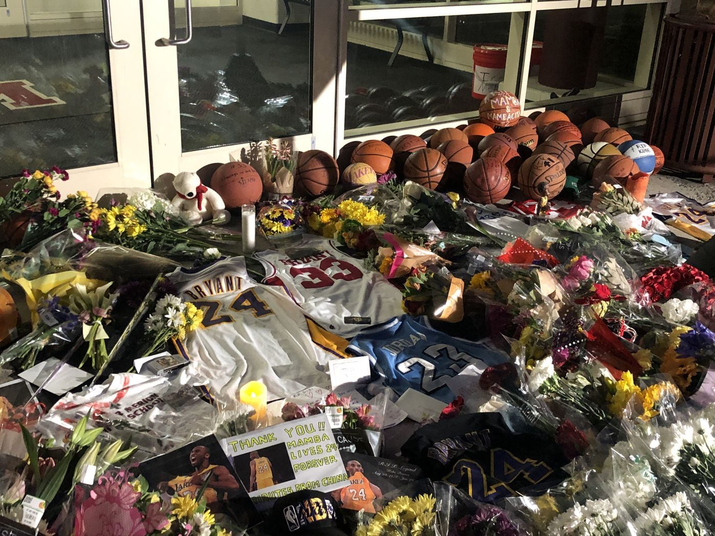 Basketball jerseys lay on the ground amid a pile of items at a makeshift memorial to Kobe Bryant outside the Bryant Gymnasium at Lower Merion High School. Among them: A Kobe Bryant No. 33 Lower Merion High School Jersey. He couldn't wear No. 33 when he played for the Lakers — the number had been retired in honor of Kareem Abdul-Jabbar.