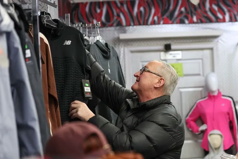 Mayor Jim Kenney picks up a black New Balance zip-up to buy at Young's Sneaker City off the West Girard Avenue commercial corridor in Brewerytown for Small Business Saturday on Nov. 25, 2023, in Philadelphia.