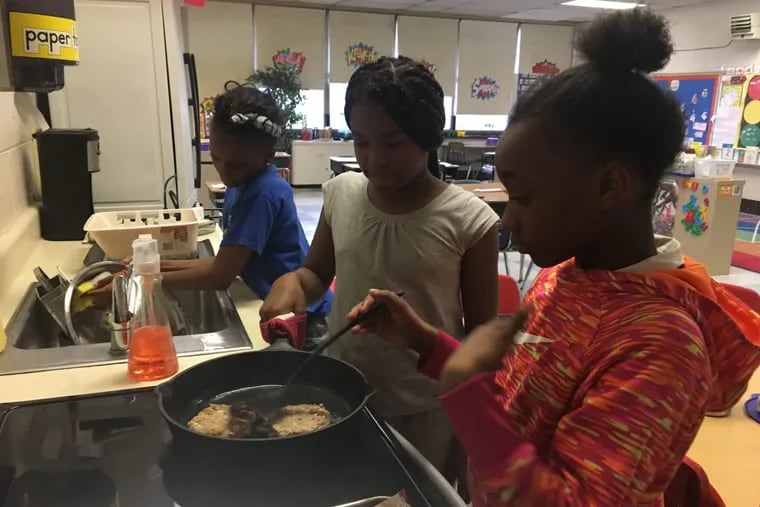 Sierrah Knox cooks turkey burgers as Makiah Green assists and Milan Blount does dishes during the My Daughter’s Kitchen cooking program at Universal Daroff Charter School in West Philadelphia.