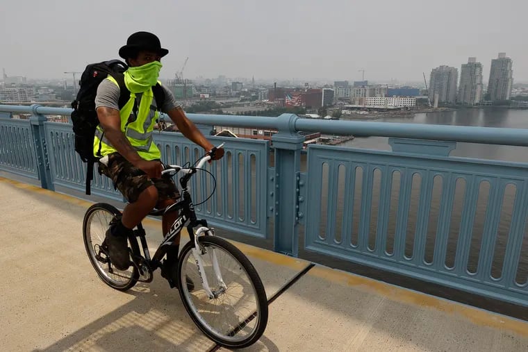 A cyclist rides with their mouth and nose covered on the Benjamin Franklin Bridge on Thursday.