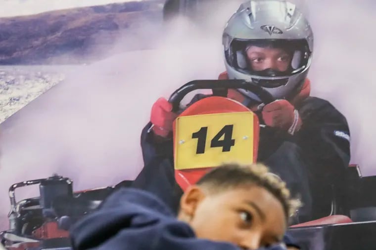 A promotional photo is seen behind Zander Whitaker as he listens to Ed Butler speak at the Urban Youth Racing School in the Fishtown section of Philadelphia on Saturday, Nov. 02, 2019. The Urban Youth Racing School is an after-school program that teaches under-served kids about engines, cars, racing, and using classes in STEM to understand the basics of mechanics and engineering in general.