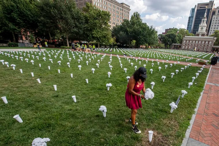 Rosalind Pichardo, who has lost multiple loved ones to gun violence, places white flowers on the lawn of Independence Hall on Monday. Seventeen hundred flowers were placed in memory of the Pennsylvanians who lost their lives to gun violence over the past year.