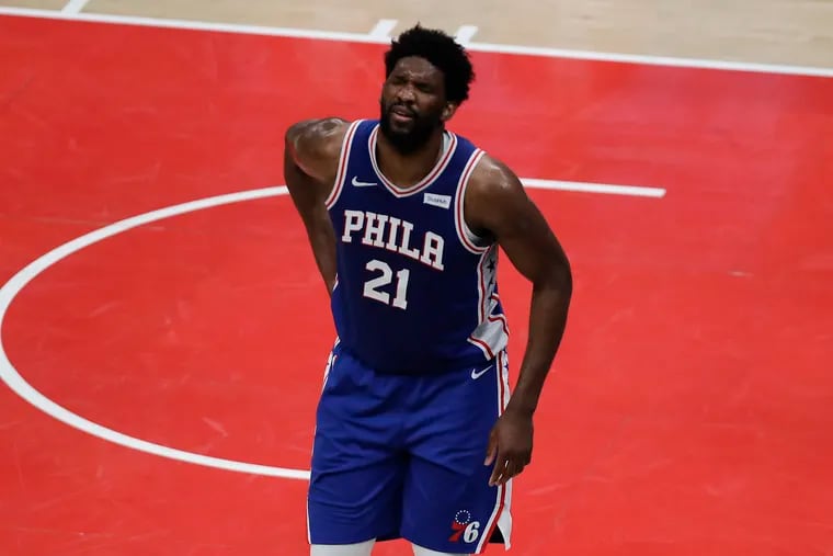 Sixers center Joel Embiid grimaces after falling down driving to the basket during the first quarter.