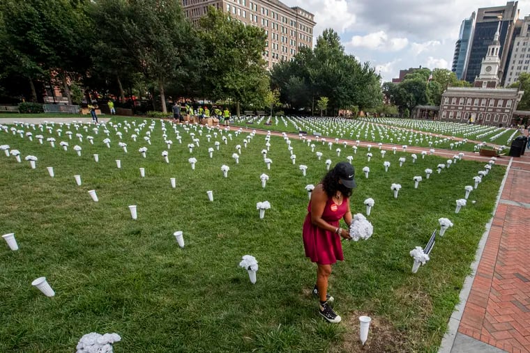 Rosalind Pichardo, violence survivor, places white flowers on the lawn of Independence Hall last month. The 1,700 roses were placed in memory of the 1,700 Pennsylvanians who lost their lives to gun violence last year.