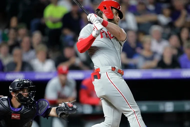 Philadelphia Phillies batter Bryce Harper, right, hits a three-run home run against the Colorado Rockies in the seventh inning of a baseball game in Denver, Saturday, April 20, 2019. Rockies catcher Drew Butera, left, reaches for the pitch. (AP Photo/Joe Mahoney)