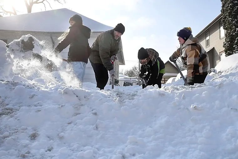 Nate LeBoutillier and his children, from left to right, Valerie, Gordie and Archie work to clear their neighbor's driveway Monday in North Mankato, Minn.