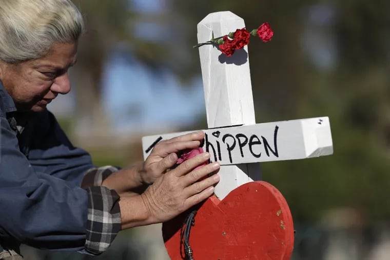 Nancy Hardy touches a flower on a cross in Las Vegas placed in honor of mass shooting victim John Phippen, of Santa Clarita, Calif.