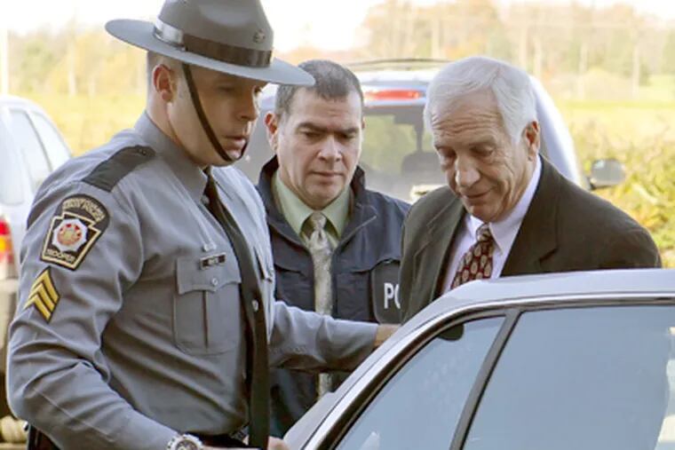 Jerry Sandusky, center, arrives in handcuffs at the office of Centre County Magisterial District Judge Leslie A. Dutchcot while being escorted by Pennsylvania State Police and Attorney General's Office officials on Saturday, Nov. 5, in State College, Pa. (AP Photo/The Patriot-News, Andy Colwell)