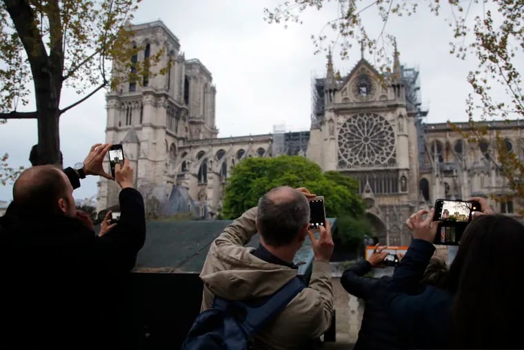 In this file photo dated Tuesday April 16, 2019, people take photos of the Notre Dame Cathedral in Paris, one day after a major blaze broke out at Paris' iconic cathedral.