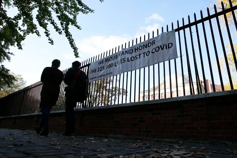 A couple on Saturday walks past a sign on a fence at the Pennsylvania Hospital mourning those who have lost their lives to the COVID-19 virus.