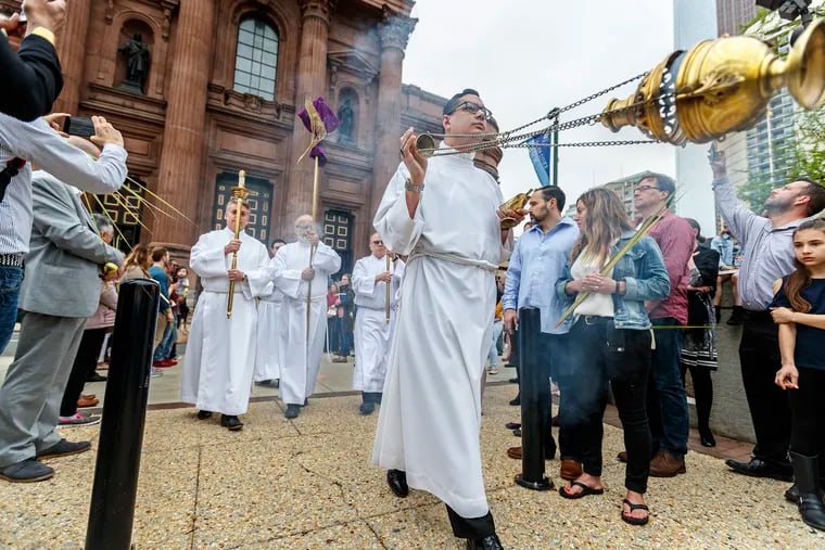 Altar server and thurifer, Adam Erdosy, swings the thurible, which contains the smoking incense, as the procession of priests makes its way through the Palm Sunday congregation gathered in Sister Citites Park to begin the Palm Sunday celebration at the Cathedral Basilica of Saints Peter and Paul on April 14, 2019.