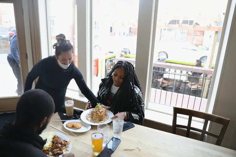 Server Jeni Cero brings food to Troy Richardson (bottom left) and his girlfriend, Siani Davis, during lunchtime at Green Eggs Cafe on Dickinson Street in South Philadelphia on Saturday, when the city allowed restaurants to reopen for indoor dining with capacity restrictions.
