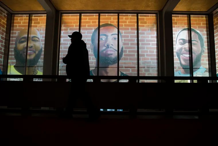 A man is silhouetted as he walks by enlargements of self-portraits made by a formerly incarcerated artists during Mural Arts Philadelphia's press preview of "Portraits of Justice" at the Municipal Services Building in Philadelphia, Wednesday, Oct. 3, 2018. The nation's largest public arts program is launching a large-scale, interactive mural in Philadelphia that focuses on solutions for mass incarceration. (AP Photo/Matt Rourke)