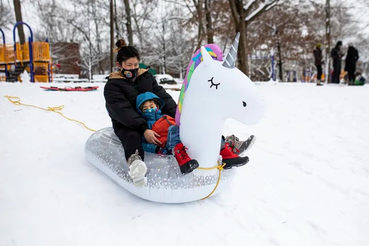 Ai Harada, of West Philadelphia, sleds down a hill in a unicorn floaty with the child she is babysitting at Clark Park in West Philadelphia, Pa., on Tuesday, Feb. 2, 2021.