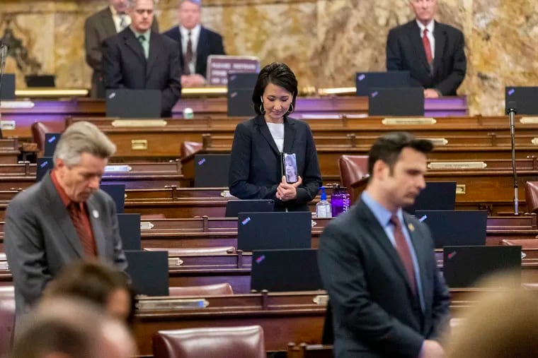 State Rep. Patty Kim (D., Dauphin) holds her cell phone up so State Rep. Maria Donatucci (D., Phila.) can see the opening prayer as State Rep. Russ Diamond (R., Lebanon) and State Rep. Andrew Lewis (R., Dauphin) bow their heads during a legislative session, Tuesday, March 24, 2020, at the Capitol in Harrisburg.