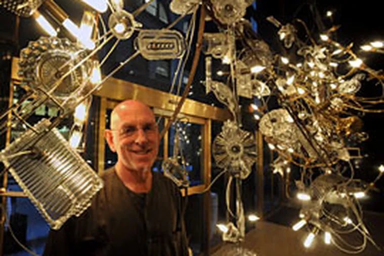 Lighting designer Warren Muller with the chandelier he created on Juniper Street. He recycles "what's available - found objects, trash."