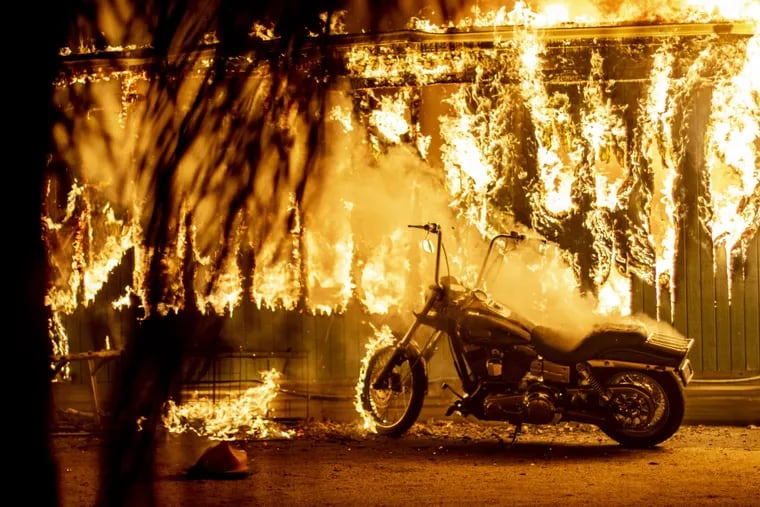 A motorcycle begins to catch fire outside an engulfed structure at a park for recreational vehicles in Malibu, California.