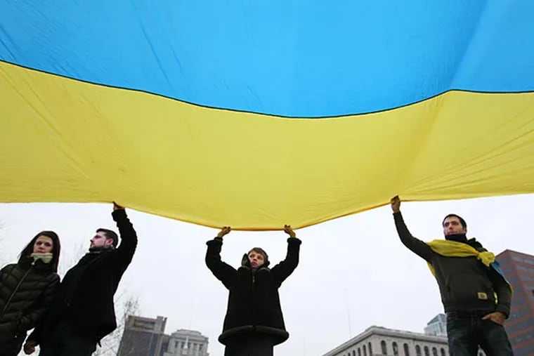 From left to right, Kristina Hontar, Nazar Ustenko, Tima Rusyn, 13, and Oleksiy Gontar all help hold up a very large Ukrainian flag during a protest over Russia's invasion of Ukraine on the Independence Mall Sunday afternoon. (MICHAEL BRYANT / Staff Photographer)