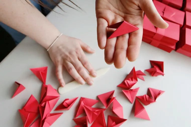 Joanna Hutchinson holds one finished origami triangle unit in her hand while outside her Philadelphia home on Sept. 26, 2020. The square pieces of paper are being packed and sent to participants who have signed up to spend hours folding origami pieces for her sculpture.