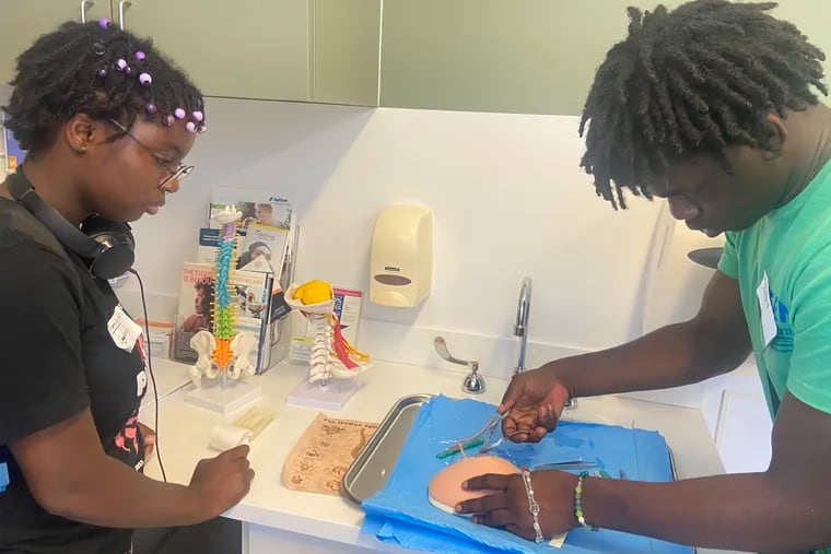 Promise Lamons watched as Decontee Moses removed surgical staples from a model of a human skull at Penn Medicine. The two Sayre High School students are part of a summer program to expose West Philadelphia teens to careers in health sciences.