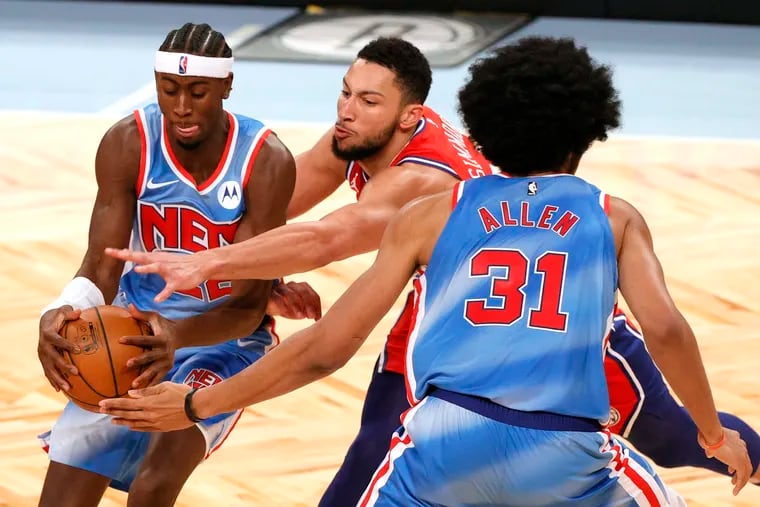 Sixer Ben Simmons (center) plays defense as Brooklyn's Caris LeVert (left) tries to drives to the basket on Thursday.