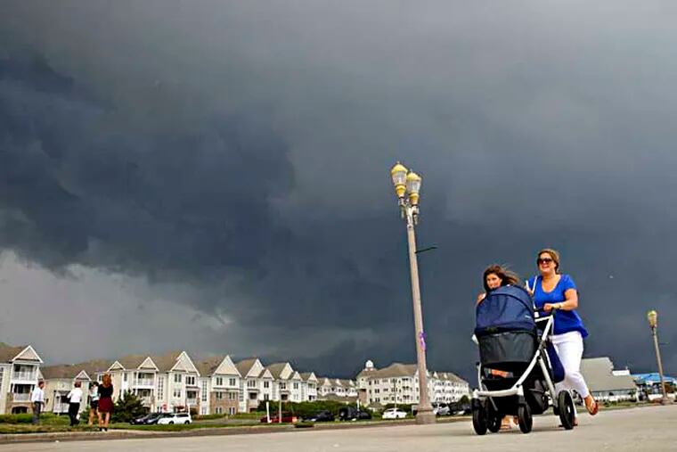 People walk along the boardwalk under dark storm clouds Tuesday, July 15, 2014, in Long Branch, N.J. A flash flood watch is in effect for many parts of the state. (AP Photo/Mel Evans)
