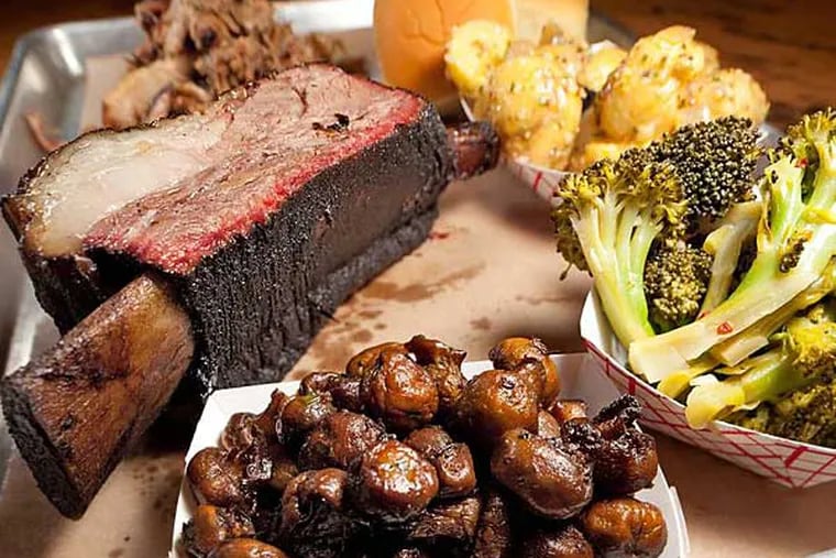 A brown paper-lined metal tray heaped with some of Fette Sau’s specialties: Black Angus bone-in short ribs, Berkshire pulled pork, rolls, German potato salad, cold Italian-style broccoli, and mushrooms.