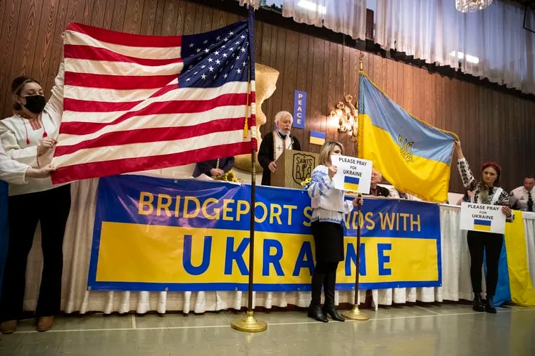 (Center) King of Prussia resident Ruslana Naida and (right) her daughter Nelya Naida, a Villanova University senior, hold the Ukrainian flag during a rally at the Saints Peter and Paul Ukrainian Catholic Church in Bridgeport, Montgomery County, on Sunday. Several hundred people attended the event to show support for Ukraine and raise funds for refugees.
