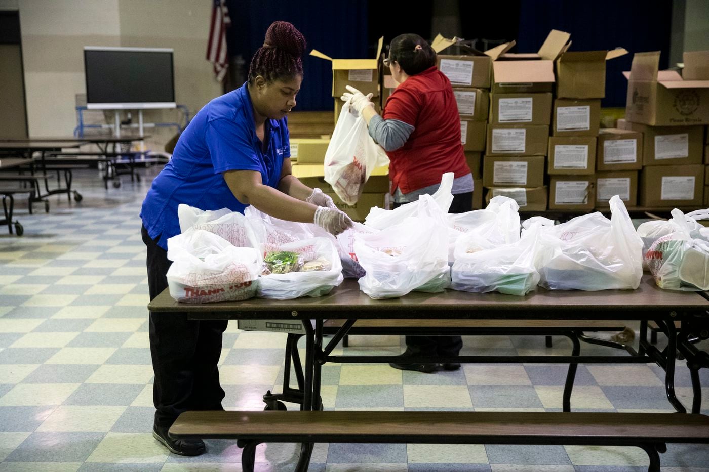 Shaleice Dudley (left), a food service worker at John H. Webster Elementary School, pasks grab-and-go meals for distribution to students and families in March after the Philadelphia School District switched to remote learning.