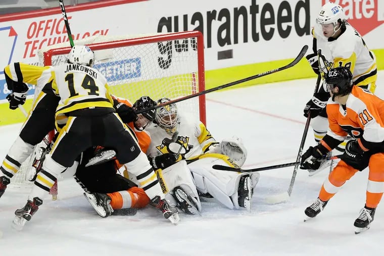 Flyers right winger Travis Konecny (right) flips the puck, which deflected off left winger Oskar Lindblom, for a goal past Pittsburgh goaltender Tristan Jarry on Wednesday. Lindblom is battling with two Penguins near Jarry.