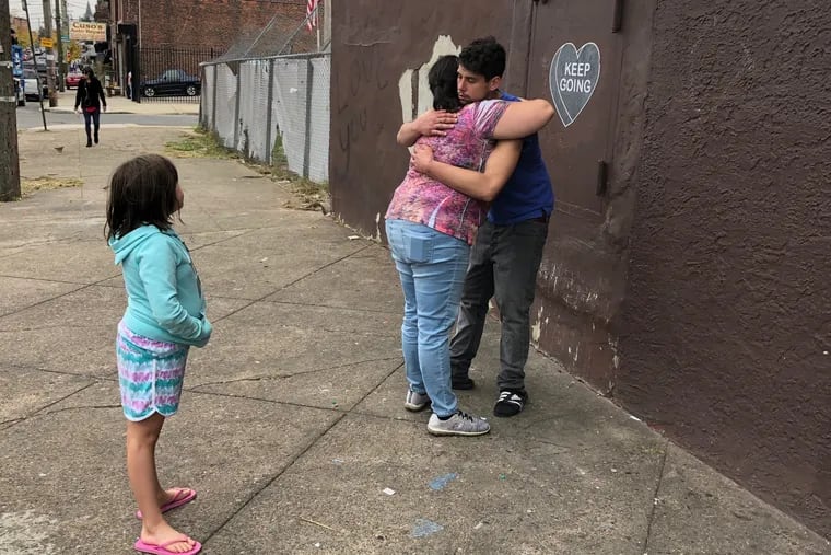 As her daughter Sarah, 8, looks on, Meredith Redmond, center, hugs her oldest daughter Rhiannon's boyfriend, at a memorial for the 22-year-old on Kensington Avenue.