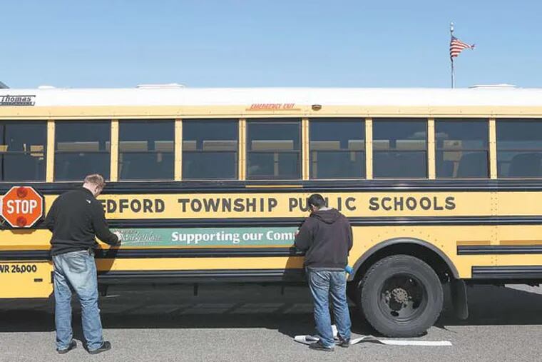 Robert Fandel (left) and Leonardo Valencia (right), sign installers, apply an advertising sign to the side of a Medford Township school bus. Fifty four school buses had the signs applied.  March 5, 2013. ( MICHAEL S. WIRTZ / Staff Photographer ).