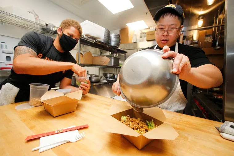 Owners of Farina Pasta and Noodle, Joe Liang (right) fills a to-go box with an order of JoeJoe Noodles as Daniel Lee prepares to add greens at their ghost kitchen in the Fairfoods Building in the Mantua neighborhood of West Philadelphia on Thursday, April 22, 2021.  The JoeJoe noodles is their version of DanDan noodles.  Lee and Liang are victims Gary Koppelman, a former president of the local food truck association and now owner of a business that supposedly fabricates food trucks.  According to several new lawsuits and the tales of many other victims, Koppelman's current business is a sham that has taken in hundreds of thousands of dollars from aspiring food truckers - but rarely, if ever, delivered the useable trucks he promised, leaving many out of their life savings and still missing their food trucking dreams.