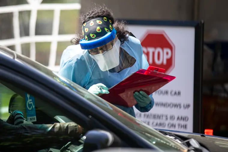 A health-care worker writes down the drivers information displayed on the dashboard of a car before testing for coronavirus in Camden on Tuesday, a coronavirus hot spot.