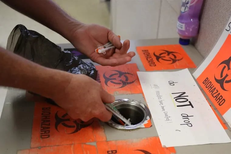 A drug user drops a series of used syringes into a wastebasket.