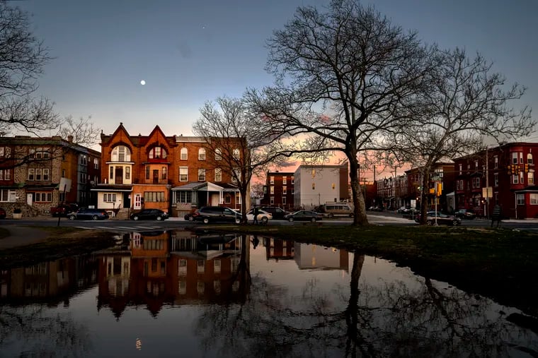 March 20, 2023: The moon rises behind the buildings along North 33rd and Oxford Streets in Strawberry Mansion as the sun sets in front of them following a day of rain.