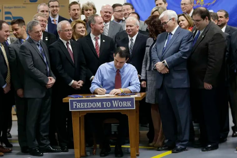 Gov. Scott Walker , at Badger Meter in Brown Deer, Wis., signs a bill into law prohibiting that workers be required to pay union dues. MIKE DE SISTI / Associated Press