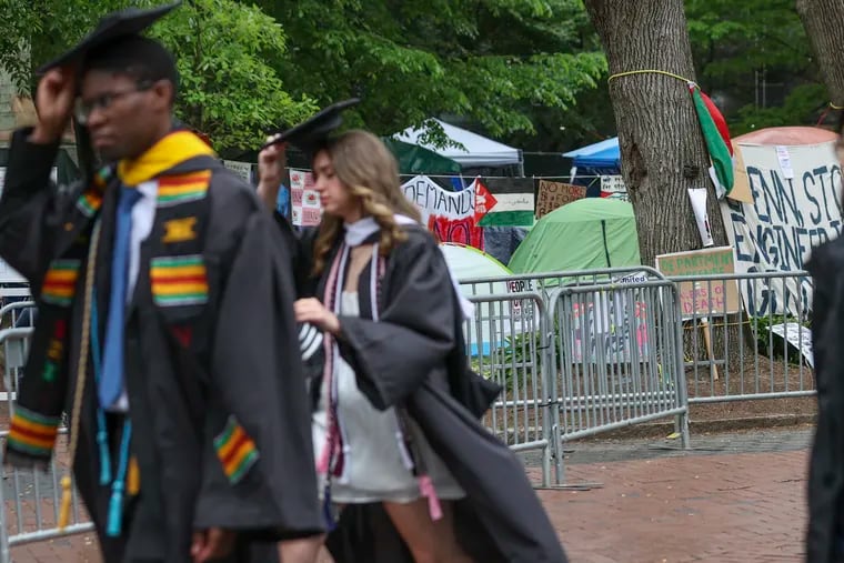 People in graduation gowns walk by the Gaza Solidarity Encampment on Penn’s campus in Philadelphia on Saturday.