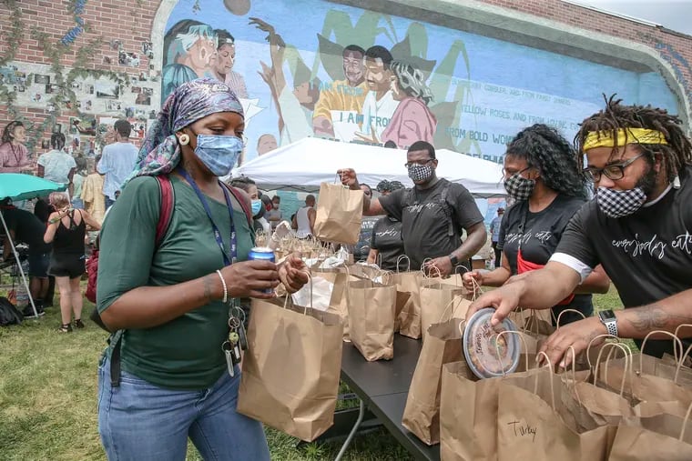 Basimah McNeal (left) picks up a food bag from chef Elijah Milligan, with help from Stephanie Wills and Kurt Evans, during a food giveaway at 52nd and Girard on June 5.