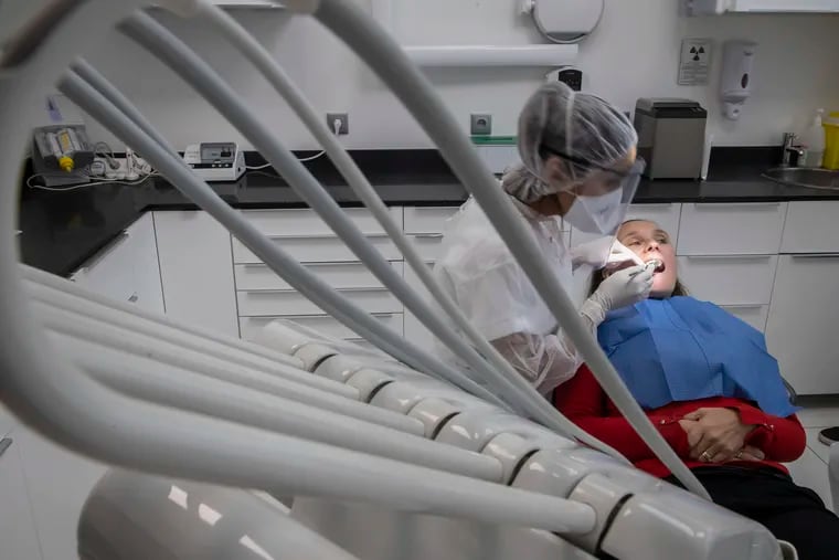 In this Wednesday, May 13, 2020 photo, dentist Sabrine Jendoubi, left, inspects the teeth of patient Veronique Guillot, during a dental appointment at a dental office in Paris. Those with toothache that suffered through France's two-month lockdown, finally have hope to end the pain. Dental practices are cautiously re-opening and non-emergency dentist appointments are now permitted around the country, as the French government eased confinement restrictions from Monday. (AP Photo/Michel Euler)