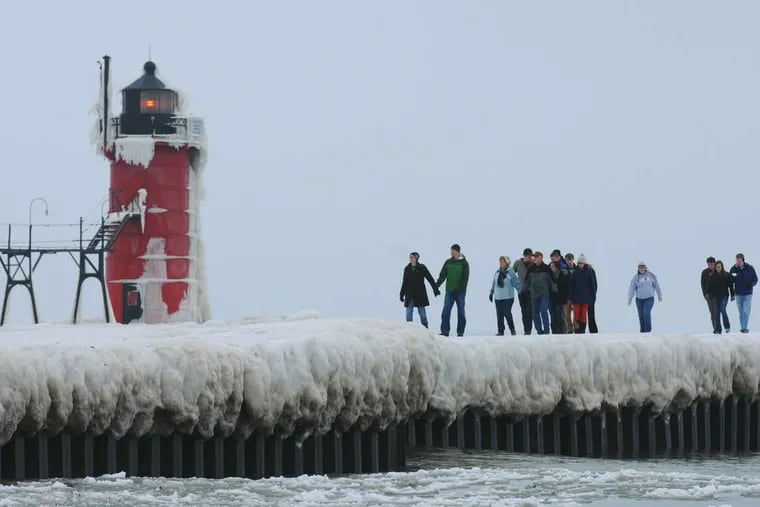 Pedestrians step along an ice-covered pier in South Haven, Mich. In Holland, Mich., a driver lost control of his car on an icy street and slammed into a hotel wall, injuring a woman inside.