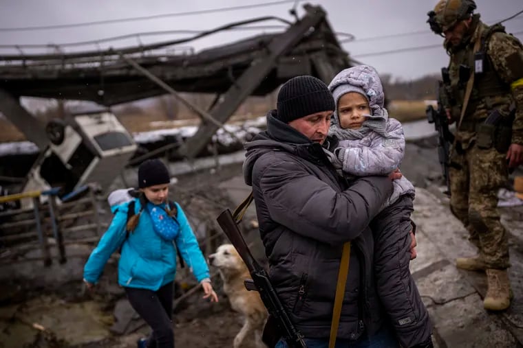 Local militiaman Valery, 37, carries a child as he helps a fleeing family across a bridge destroyed by artillery, on the outskirts of Kyiv, Ukraine, Wednesday, March 2. 2022. Russian forces have escalated their attacks on crowded cities in what Ukraine's leader called a blatant campaign of terror.