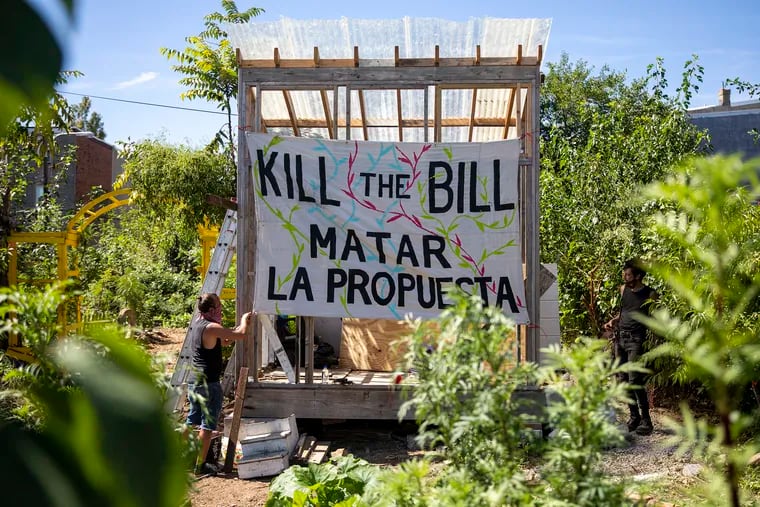 John Mulligan, a Bucks County resident and volunteer in this North Philadelphia community garden, puts up a banner urging locals to stand against City Council taking community gardens and other community-held lands in the area.